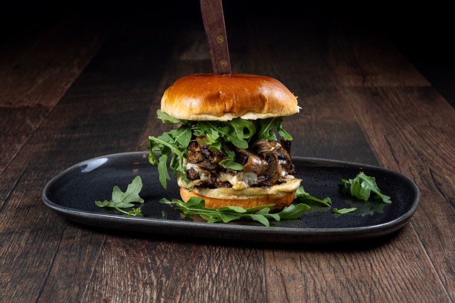 Hamburguesa The Swiss Trifolati con champiñones, queso suizo derretido y rúcula en un plato negro, Ozys Tavern