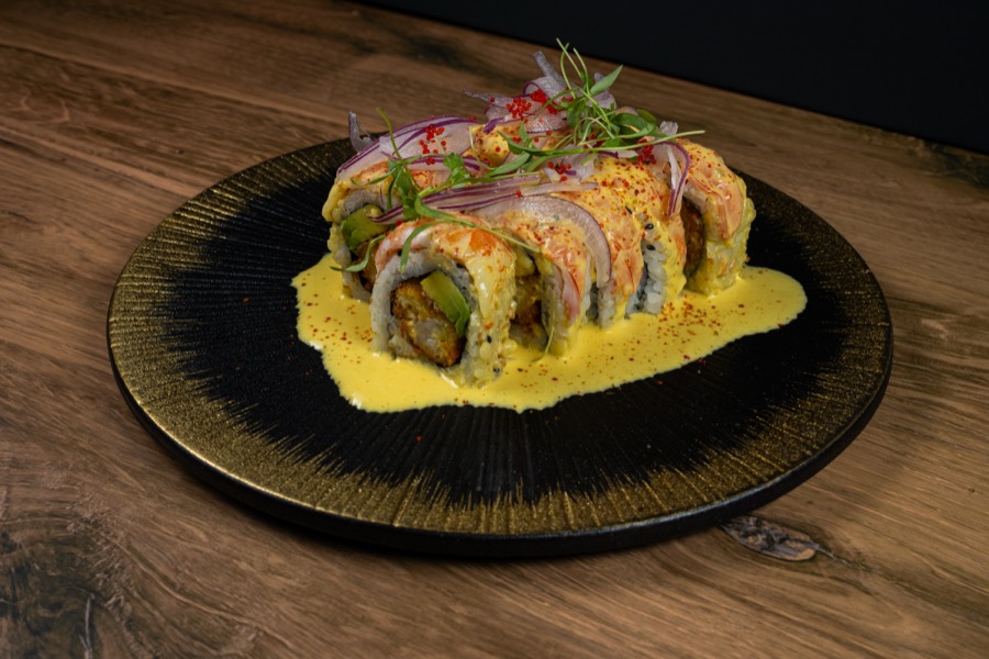 Rollo de sushi con salsa amarilla en un plato negro y dorado