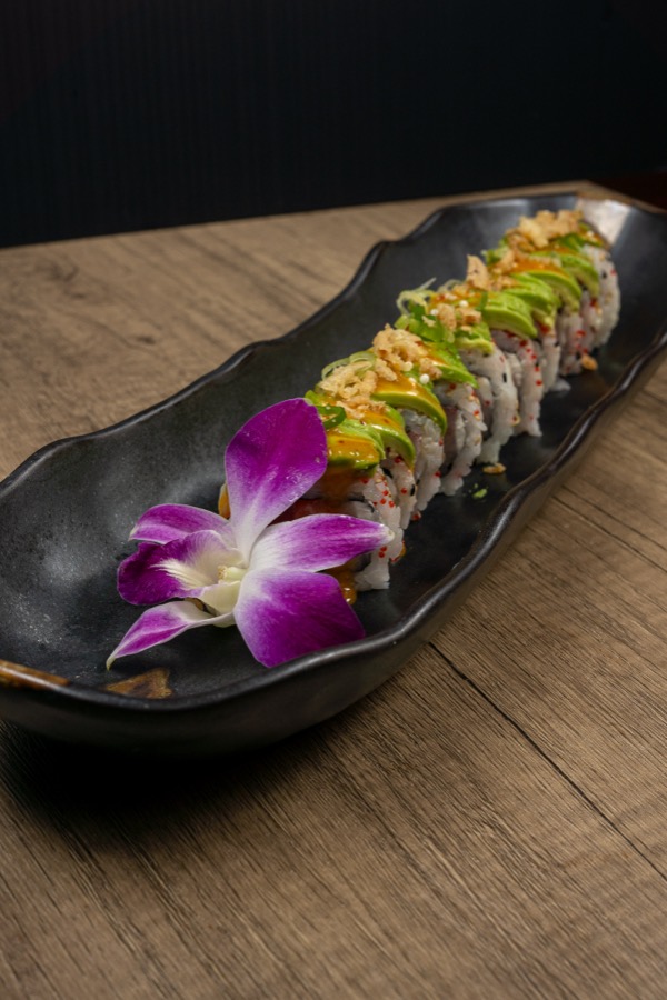 Rollo de sushi con aguacate y una orquídea morada