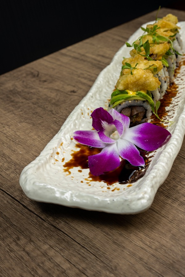 Rollo de sushi con salsa de anguila y una orquídea